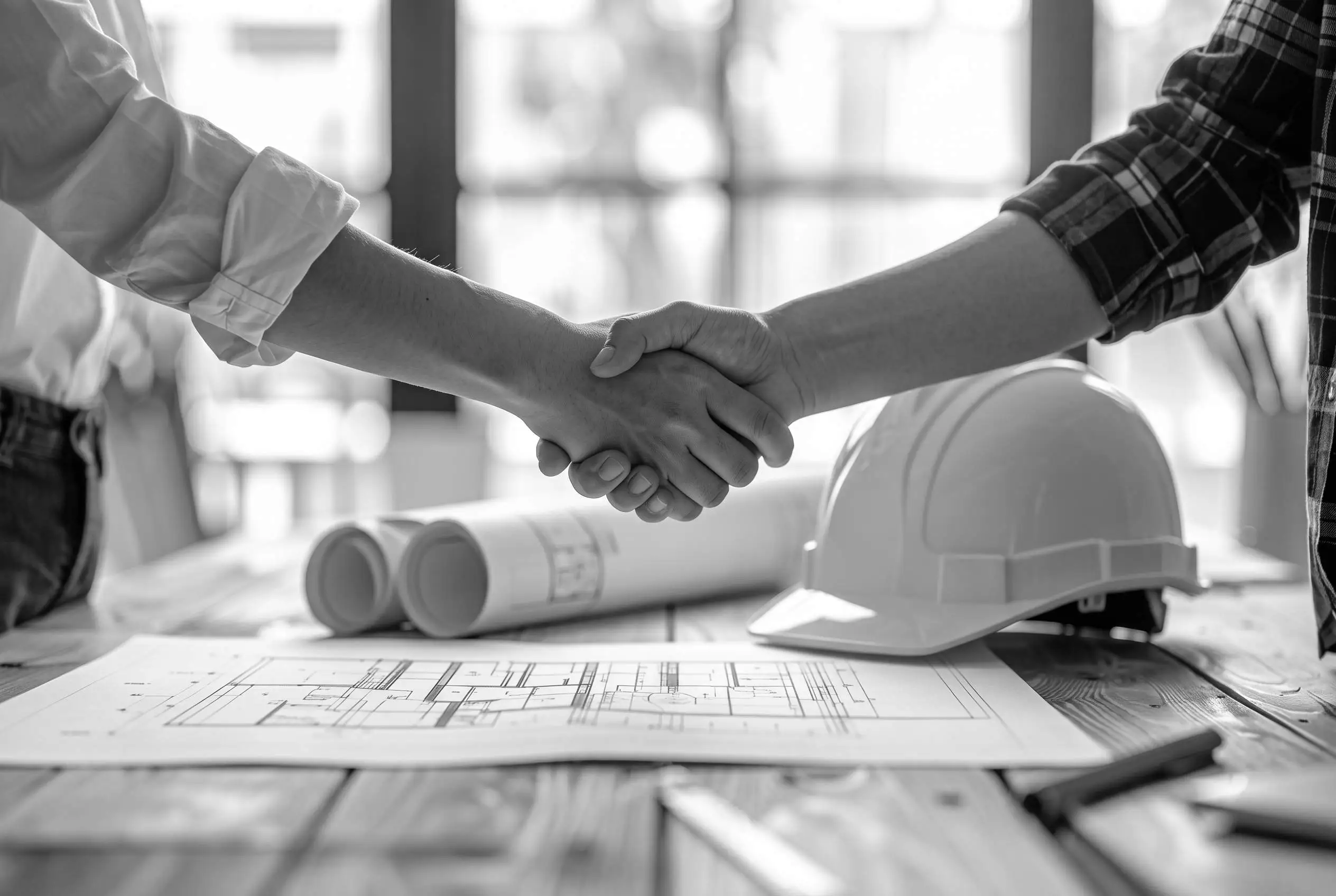 Stretta di mano tra un architetto e un referente dedicato BEHOME su una scrivania con piantine e caschetto, a simboleggiare la solida partnership e la stretta collaborazione offerta ai professionisti del settore.