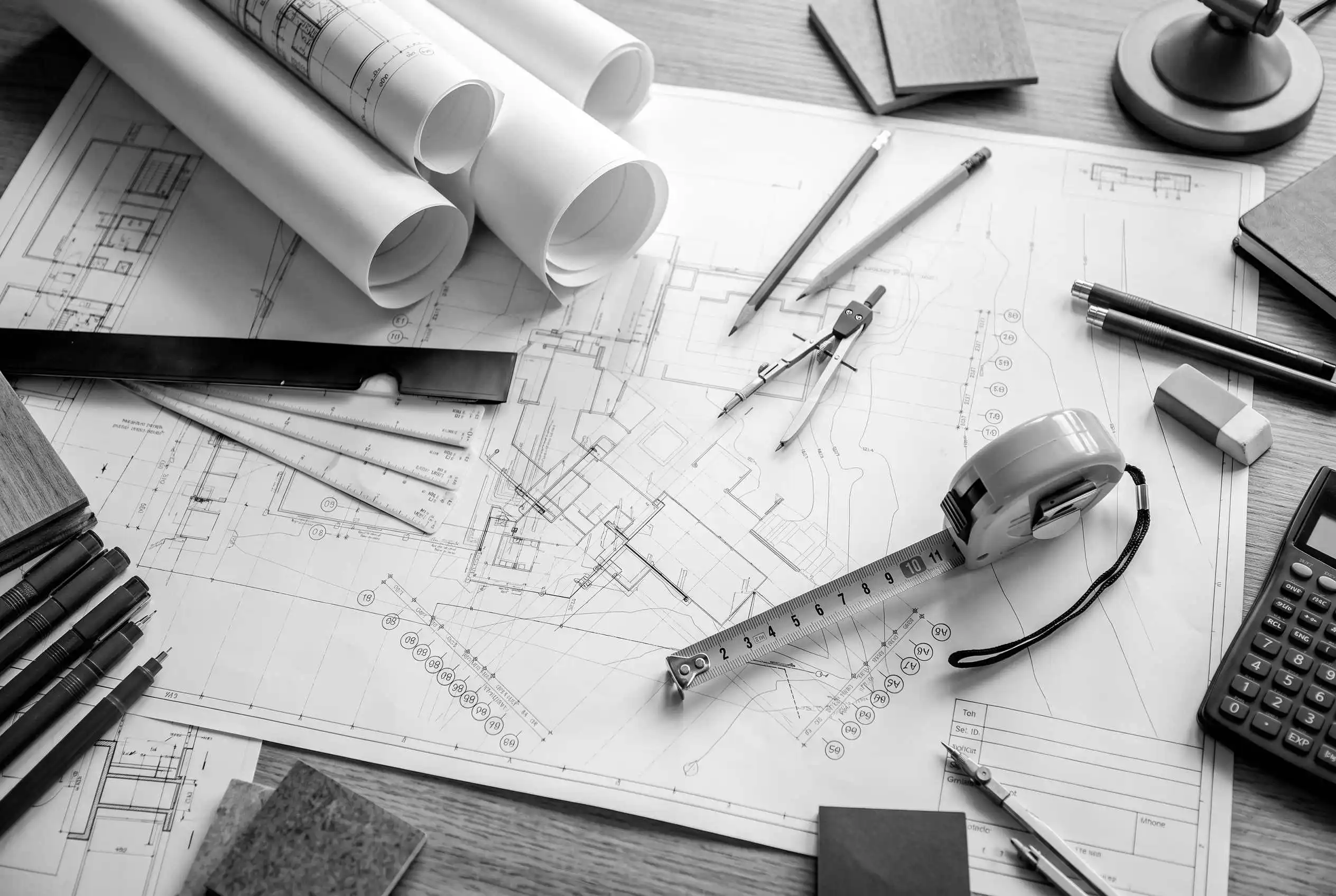 Vista dall'alto di un tavolo da lavoro con piantine architettoniche, metro, compasso e strumenti da disegno, che simboleggiano lo studio accurato degli spazi e la progettazione su misura firmata BEHOME.
