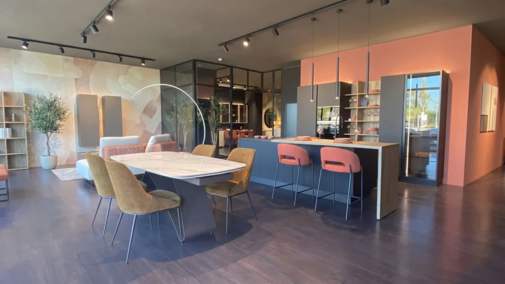Esposizione della zona living e cucina moderna all'interno del nuovo negozio BEHOME a Grosseto, con tavolo da pranzo, sedie colorate e penisola.
